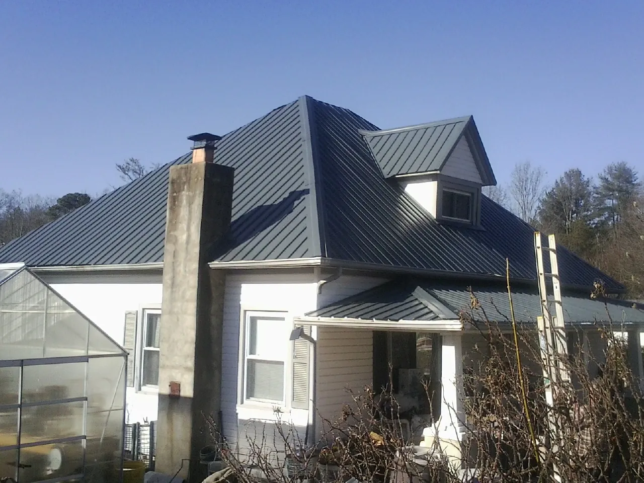 Dark blue standing seam metal roof on a white farmhouse with dormer — Slate & Tile Roof Repair by Roofing Brothers in Onalaska