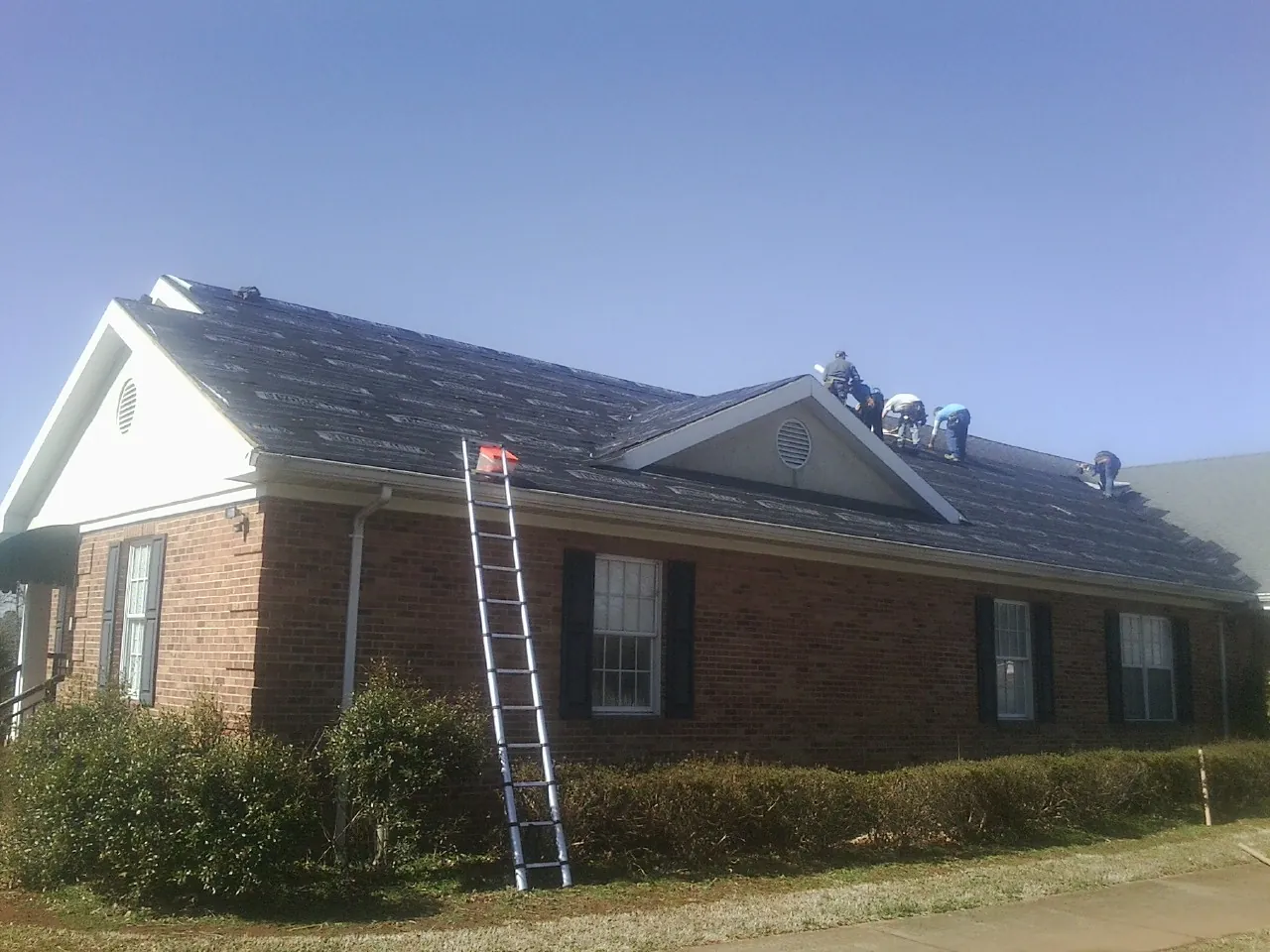 Crew tearing shingles off a brick ranch roof with a ladder set — Emergency Roof Repair work by our crew in Onalaska