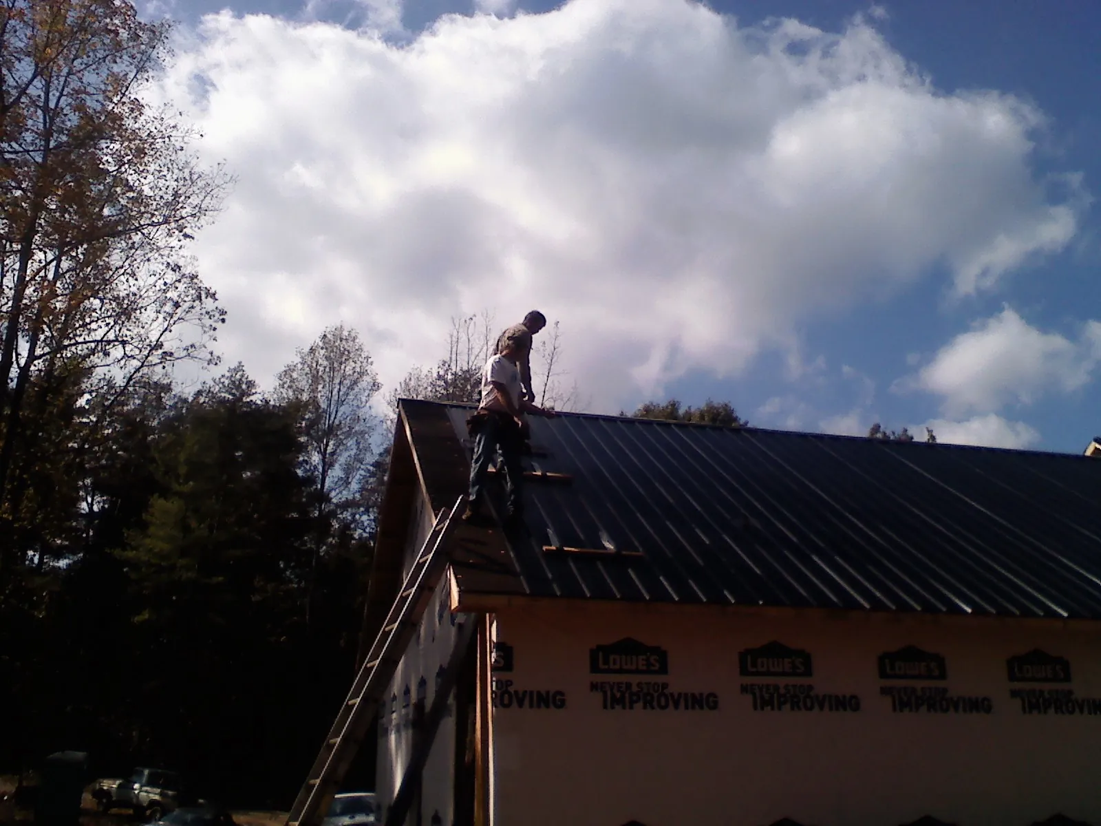Roofer fastening dark metal panels high against a cloudy sky, from a Roof Inspection job in Onalaska