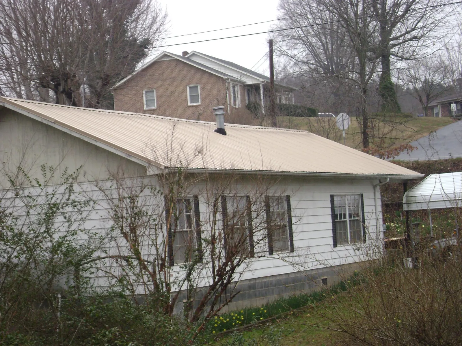 Tan metal roof on a white sided house set into a hillside — Commercial Roofing by Roofing Brothers in Onalaska